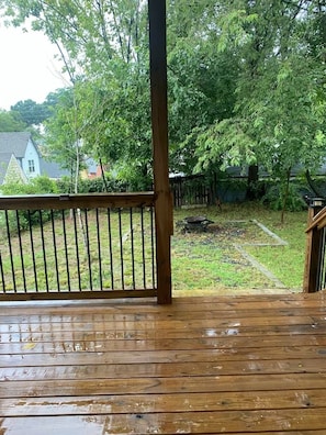 A wooden deck with a metal railing, a grassy yard, and trees in the background.
