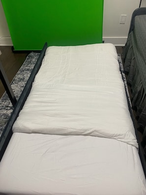 A bed with a white mattress in a room with a green wall and a power outlet.