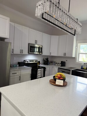 A modern kitchen with white cabinetry, stainless steel appliances, and a central island with a fruit bowl.