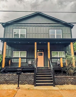 A two-story building with a front porch, a door, and a staircase leading to the entrance.