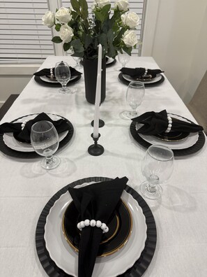 Ein Tisch für vier Personen, gedeckt mit schwarz-weißen Tellern, klaren Gläsern und einer Vase mit weißen Blumen.