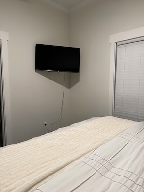 A bedroom with a bed, a wall-mounted television, and a window with blinds.