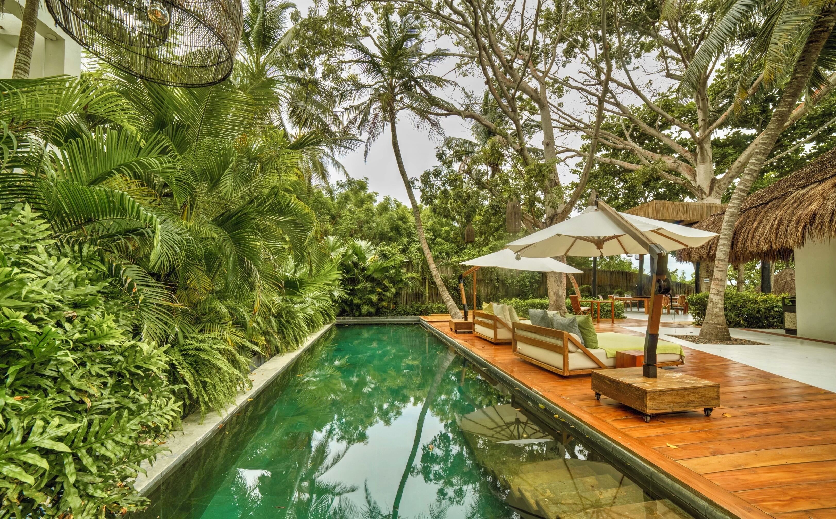 A poolside area with a wooden deck, lounge chairs, and umbrellas.