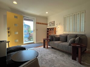 Ein Wohnzimmer mit Sofa, Couchtisch, einer Tür und einem Fenster mit Rollläden.