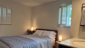 A bedroom with a bed, bedside lamps, a nightstand, a window with blinds, and a bathroom with a sink. - Hyde Park "Rail Trail" Entire House (Cincinnati)