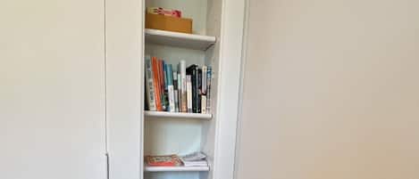 Una silla de madera con un tapete de corte azul sobre una mesa, un estante blanco con libros y recipientes, y una puerta blanca.