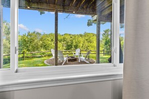 Blick aus dem Fenster auf eine Holzterrasse mit Adirondack-Stühlen und einer Feuerstelle.