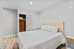 Ein Schlafzimmer mit Bett, Nachttisch, Lampe und einem Kleiderschrank mit Spiegel.