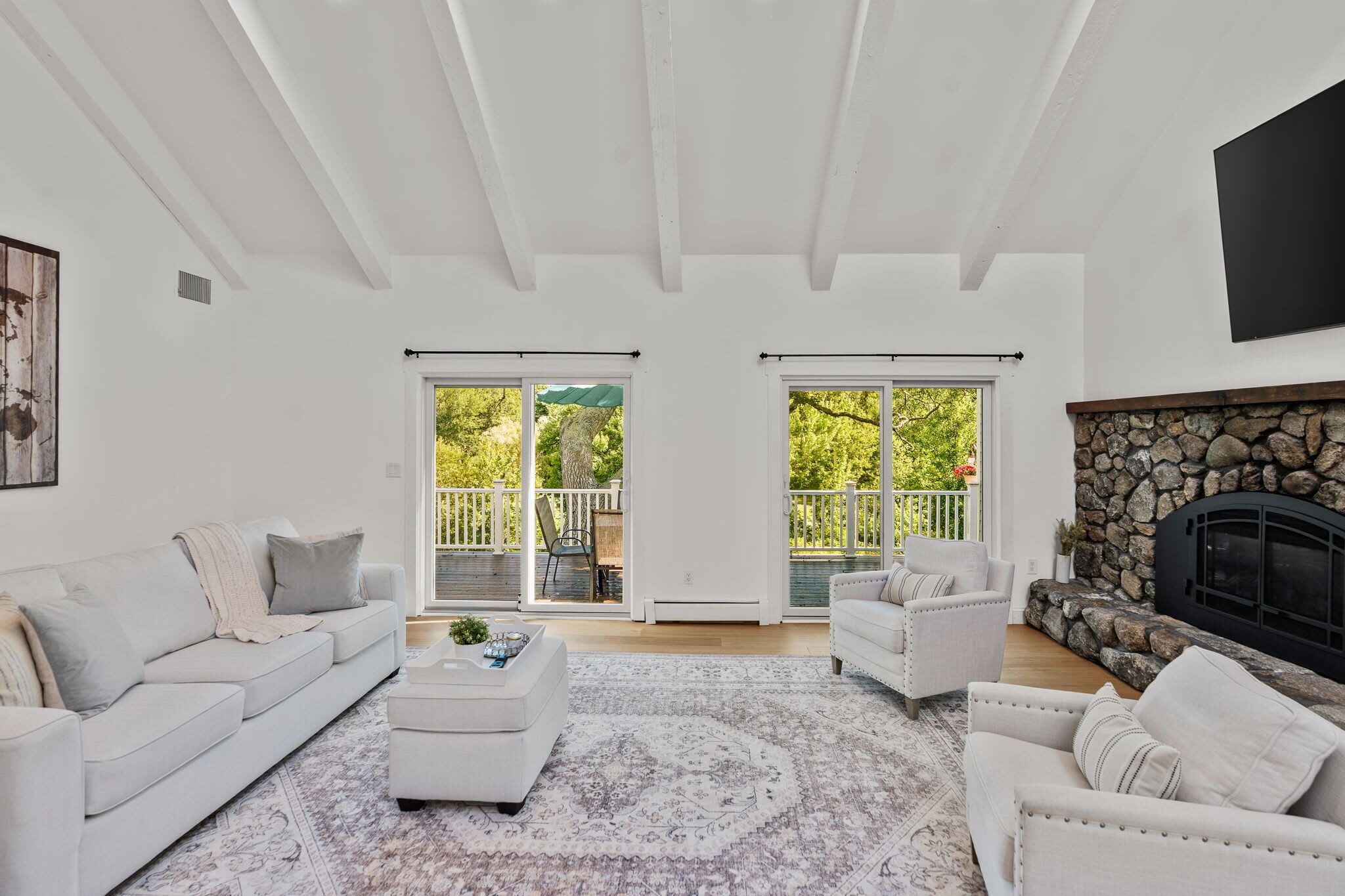 A spacious living room with a fireplace, a white sofa, a coffee table, and a view of the outdoors through large windows.
