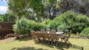 A wooden table and chairs set outdoors with dense shrubbery and trees in the background. - Behind the Dunes - Point Lonsdale (Point Lonsdale)