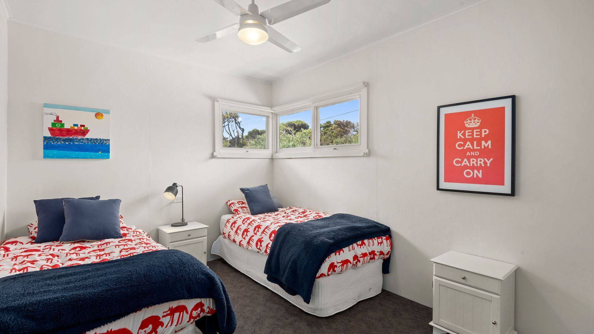 A bedroom with two beds, a nightstand, a desk, a window, and a ceiling fan.