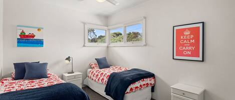 A bedroom with two beds, a nightstand, a desk, a window, and a ceiling fan.
