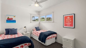 A bedroom with two beds, a nightstand, a desk, a window, and a ceiling fan. - Behind the Dunes - Point Lonsdale (Point Lonsdale)