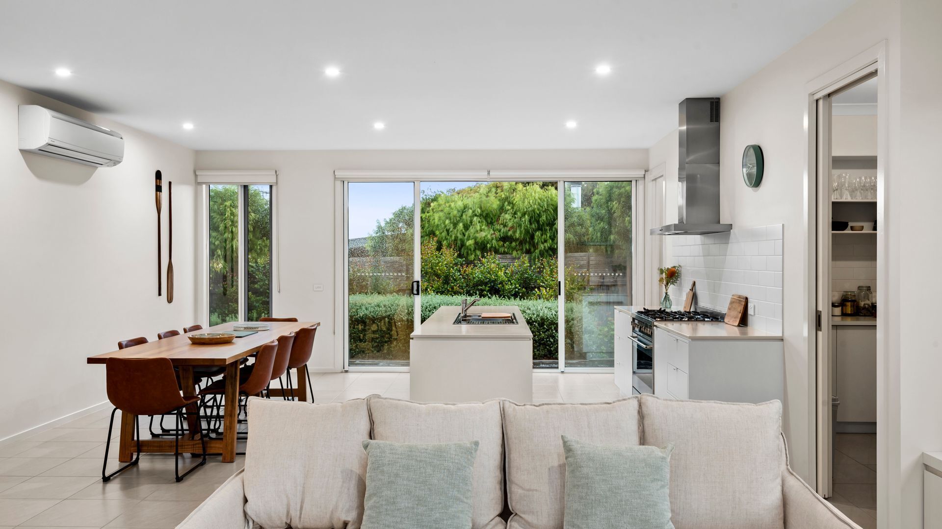A modern kitchen with a built-in stove, a dining area with a wooden table and chairs, and a large sliding glass door leading to a garden.