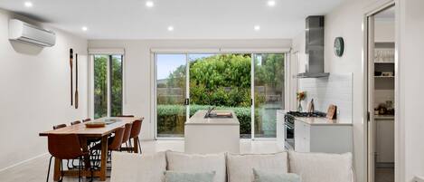 A modern kitchen with a built-in stove, a dining area with a wooden table and chairs, and a large sliding glass door leading to a garden.