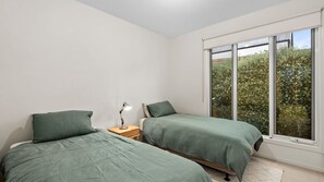 Ein Schlafzimmer mit zwei Betten, einem Nachttisch und einem Fenster mit Blick auf Bäume.
