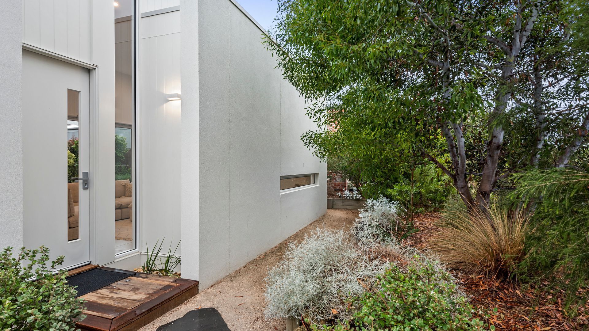 A modern building with a white exterior, a glass door, and a small outdoor seating area with a bench and cushions.