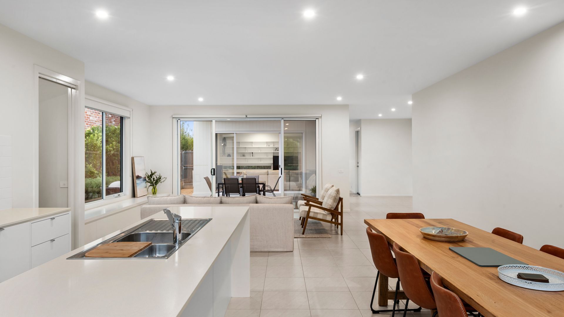A modern kitchen with a central island, a dining area with a wooden table and chairs, and a view of a garden through glass doors.