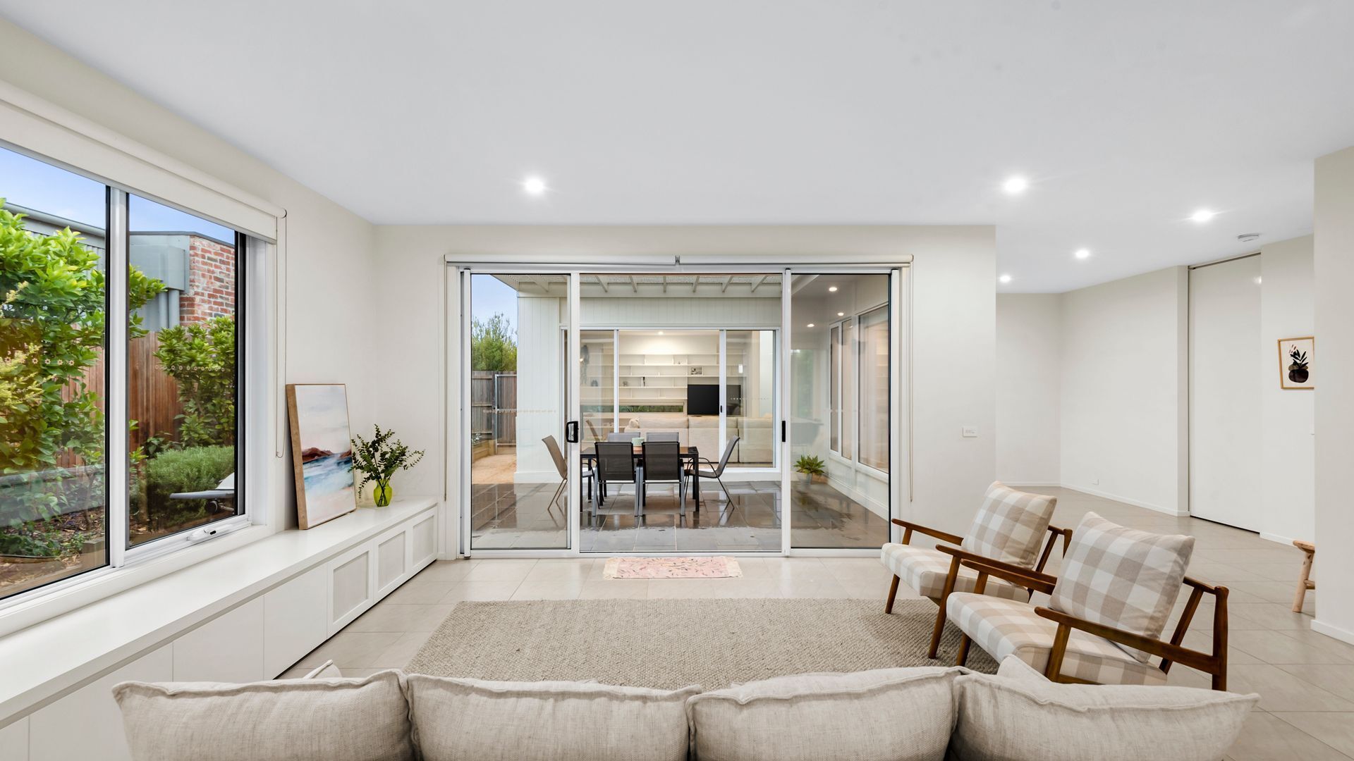 A modern living room with a large sliding glass door leading to an outdoor dining area.