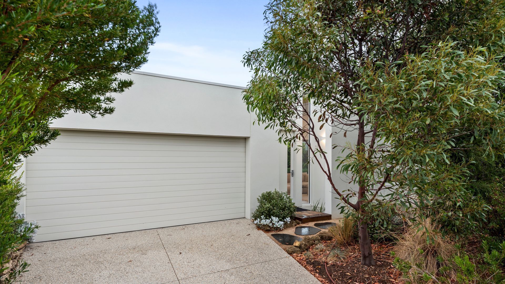 A modern house with a garage, a small garden with a tree, and a paved driveway.