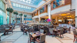 Un espacio interior amplio con varias mesas y sillas para comer, una zona de bar central y un techo alto con tragaluces.