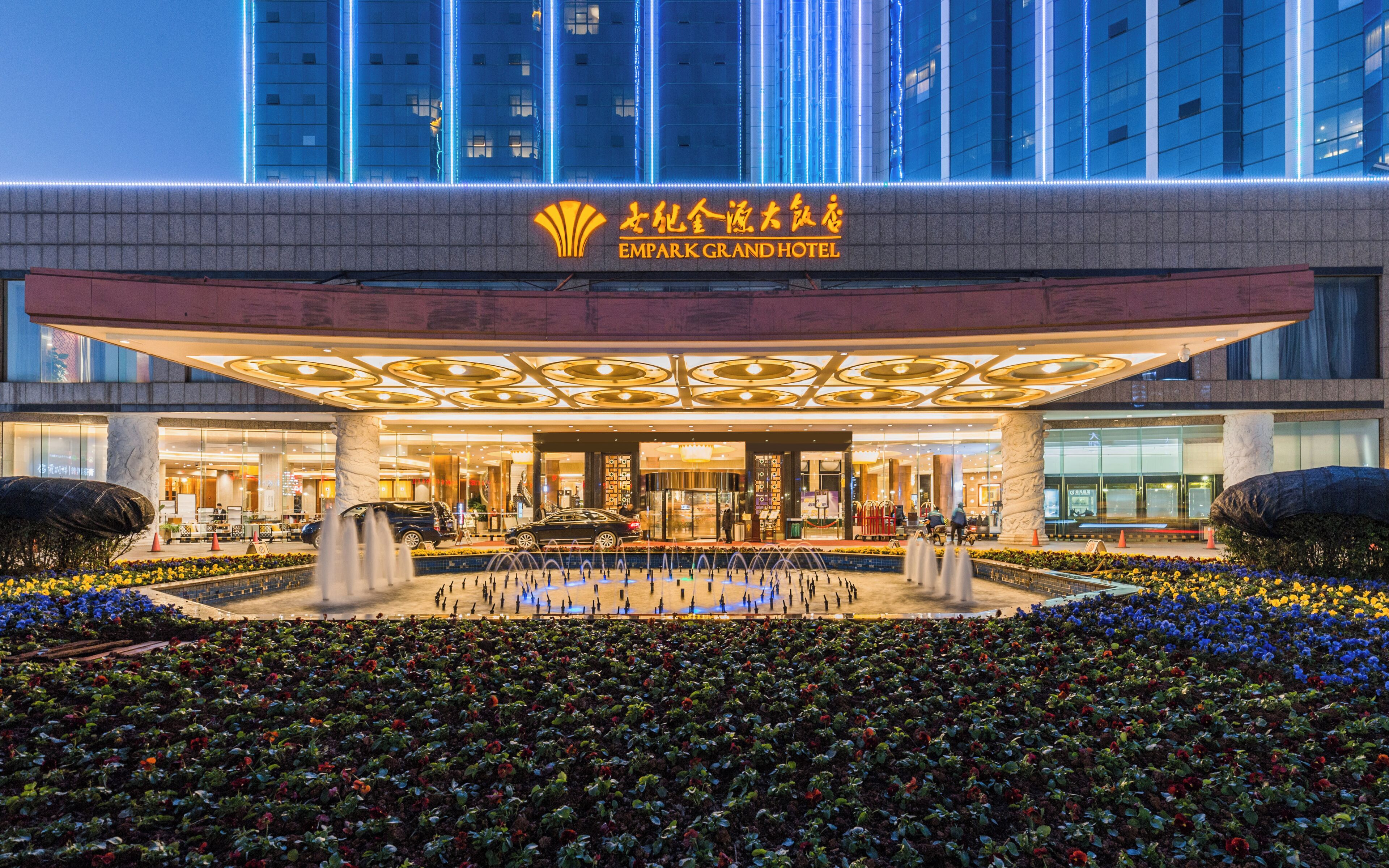 The exterior of the Empark Grand Hotel with a large entrance, a fountain, and a flower garden.