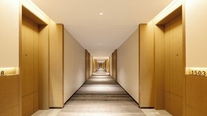Un pasillo de hotel con puertas de madera, carteles de números de habitación y piso alfombrado.