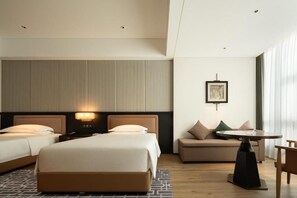 A hotel room with two beds, a sofa, a table, and a picture on the wall.
