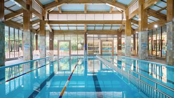 Una amplia piscina interior con carriles delimitados, rodeada de pilares de piedra y vigas de madera.