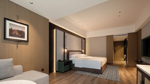 Habitación de hotel moderna con una cama grande, zona de estar, escritorio y baño visible a través de una puerta abierta.