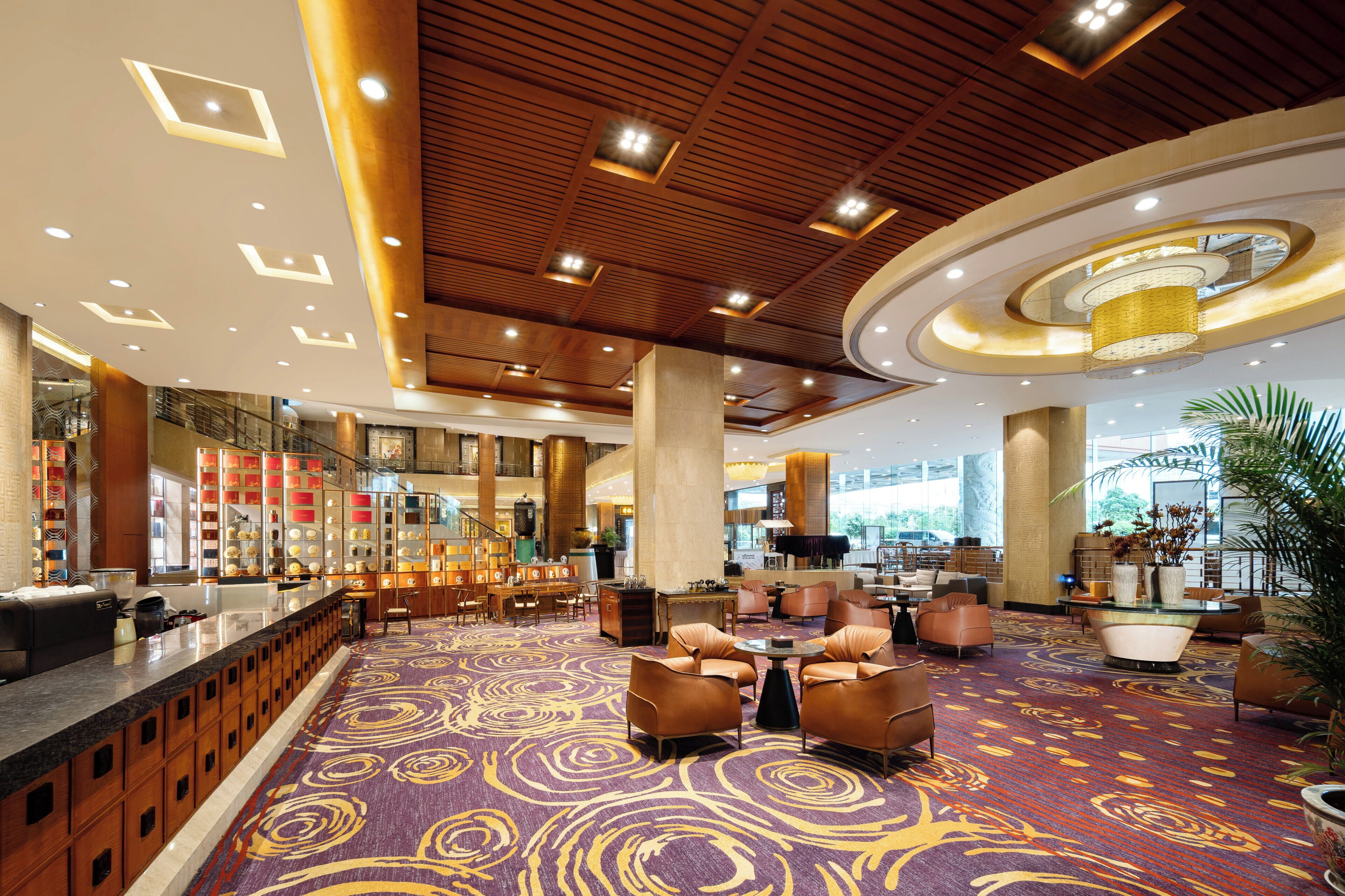 Vestíbulo de hotel con zona de estar central, mostrador de recepción y un amplio ventanal con vistas al exterior.