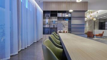 A modern conference room with a long table, green chairs, and a bookshelf with books and decorative items.