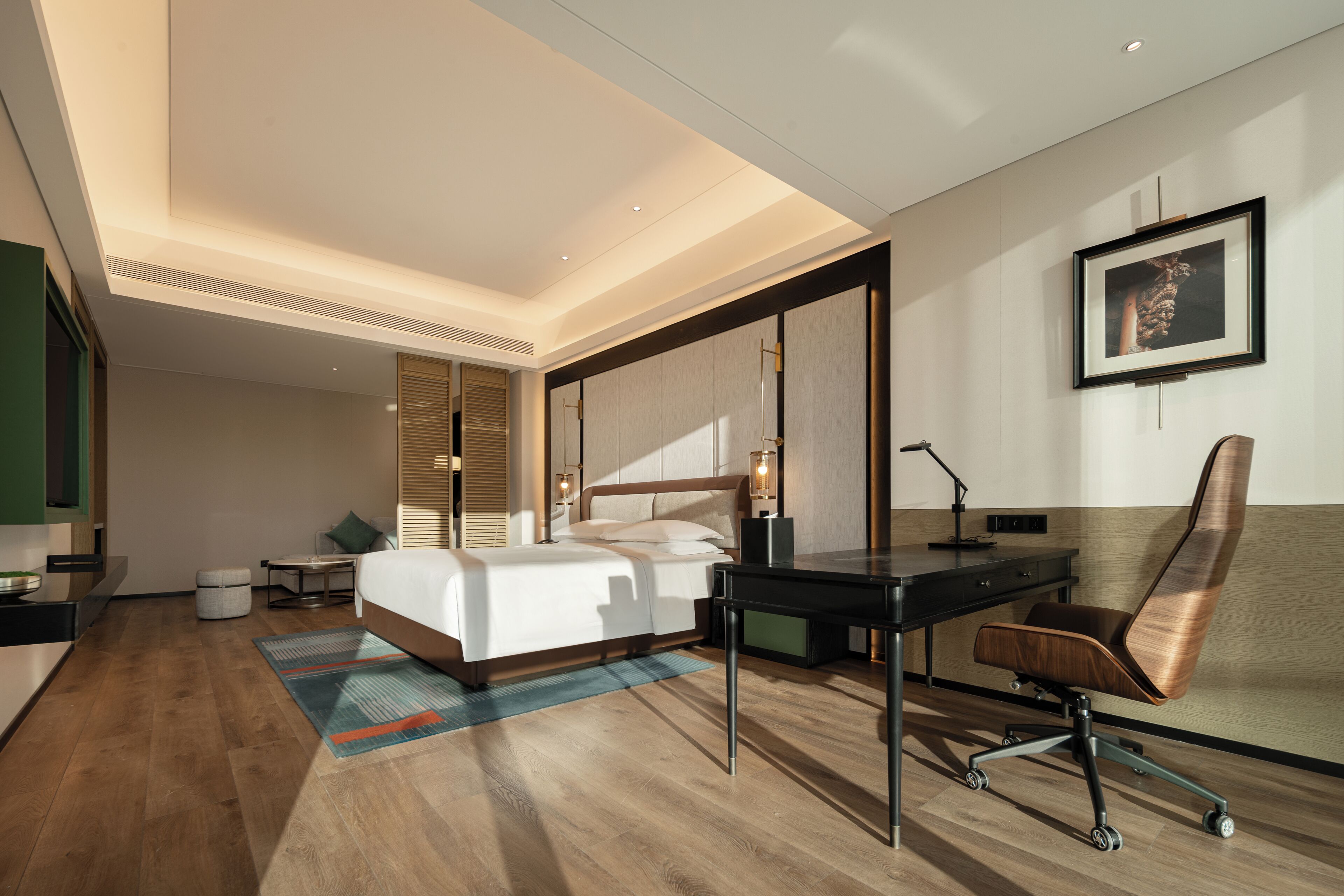 A modern hotel room with a bed, desk, chair, and a framed picture on the wall.