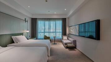 Habitación de hotel con dos camas, un sofá, una mesita y un ventanal grande con cortinas.