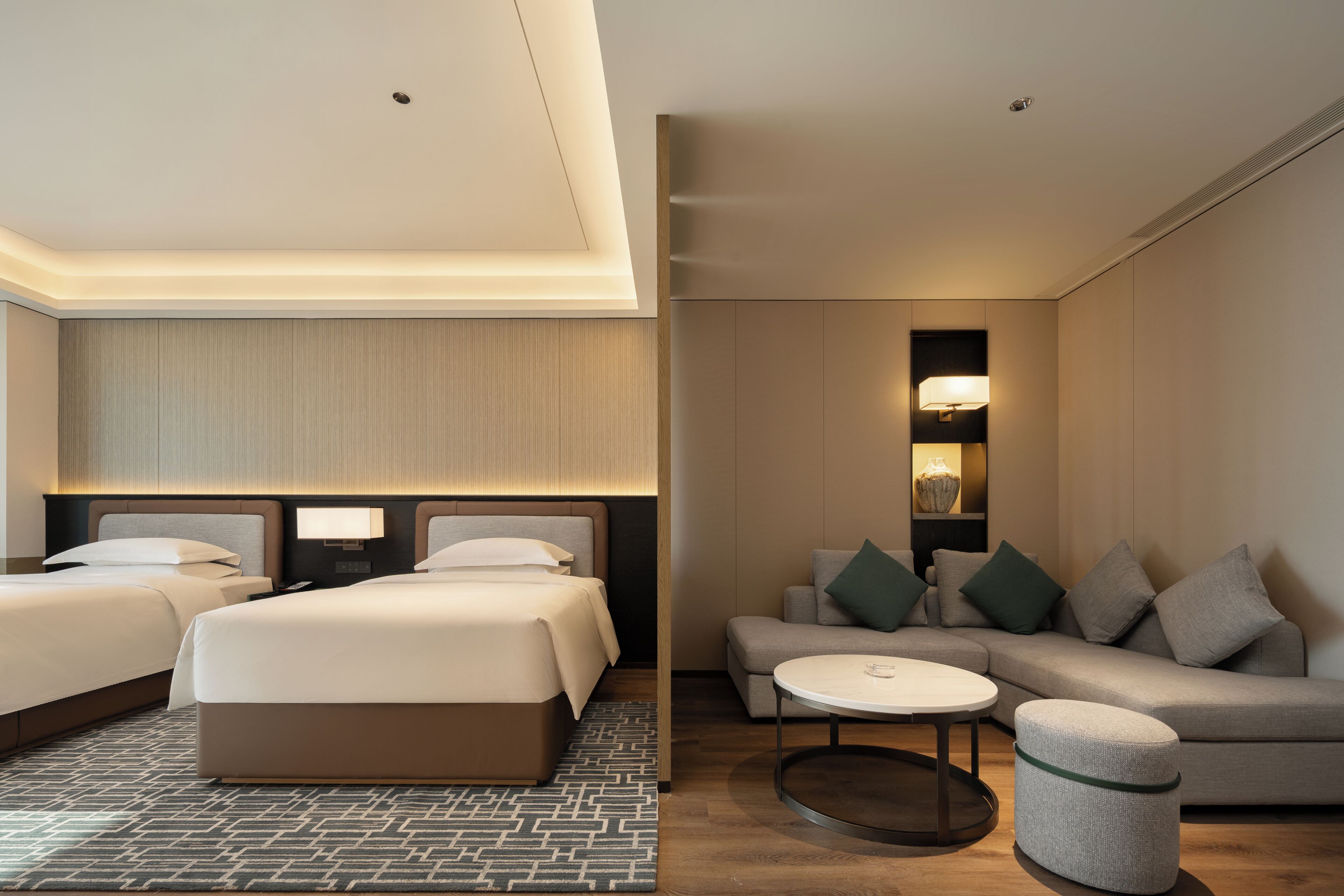 A hotel room with two beds, a sofa, a small table, and a round ottoman.