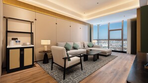 Habitación de hotel moderna con sofá, sillones, una mesa de centro y vista a la ciudad a través de amplias ventanas.