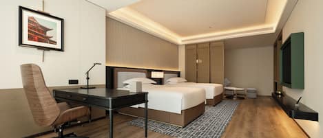 A modern hotel room with a desk, two beds, a chair, a TV, and a framed picture on the wall.