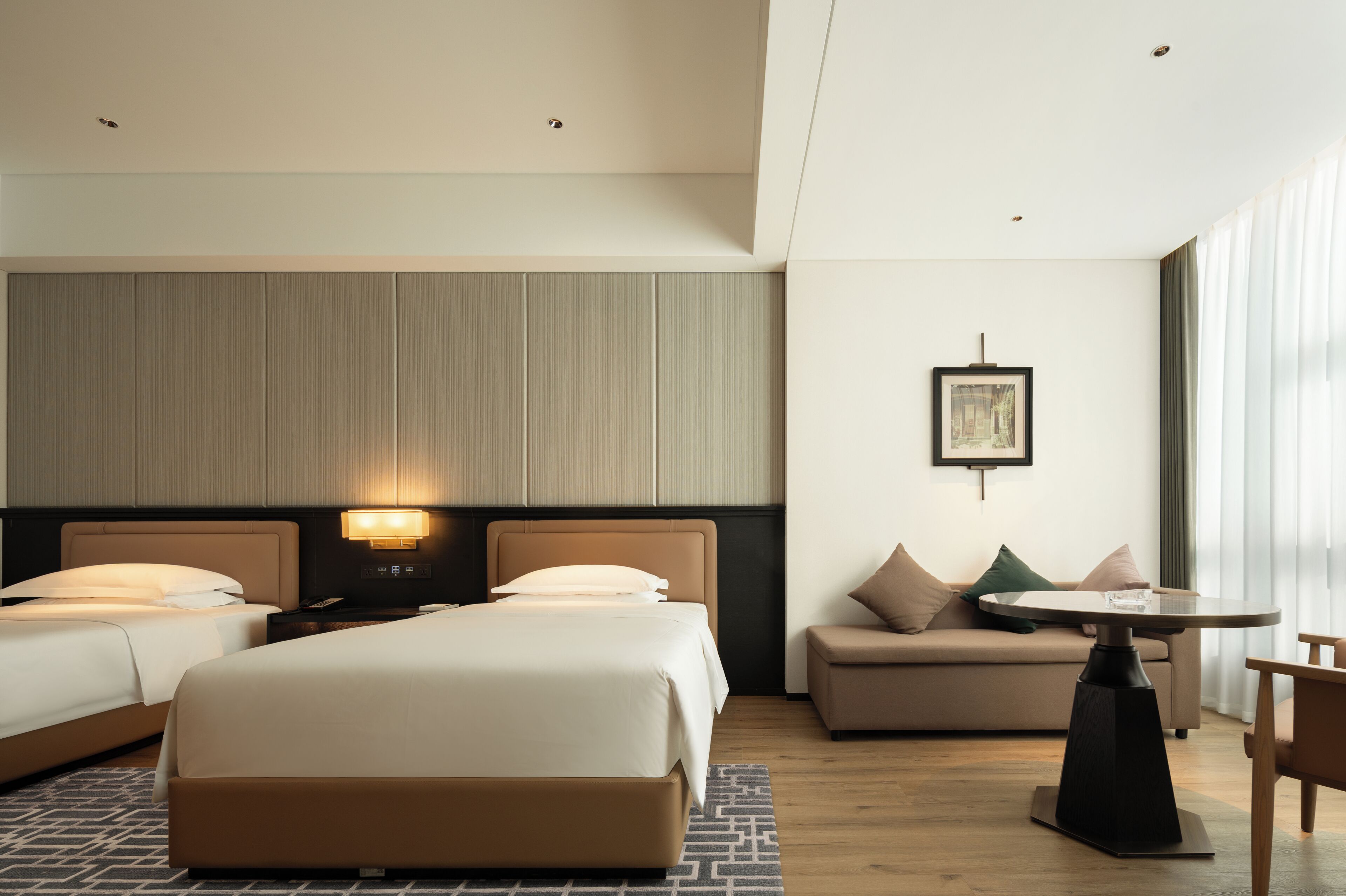A hotel room with two beds, a sofa, a small table, and a picture on the wall.