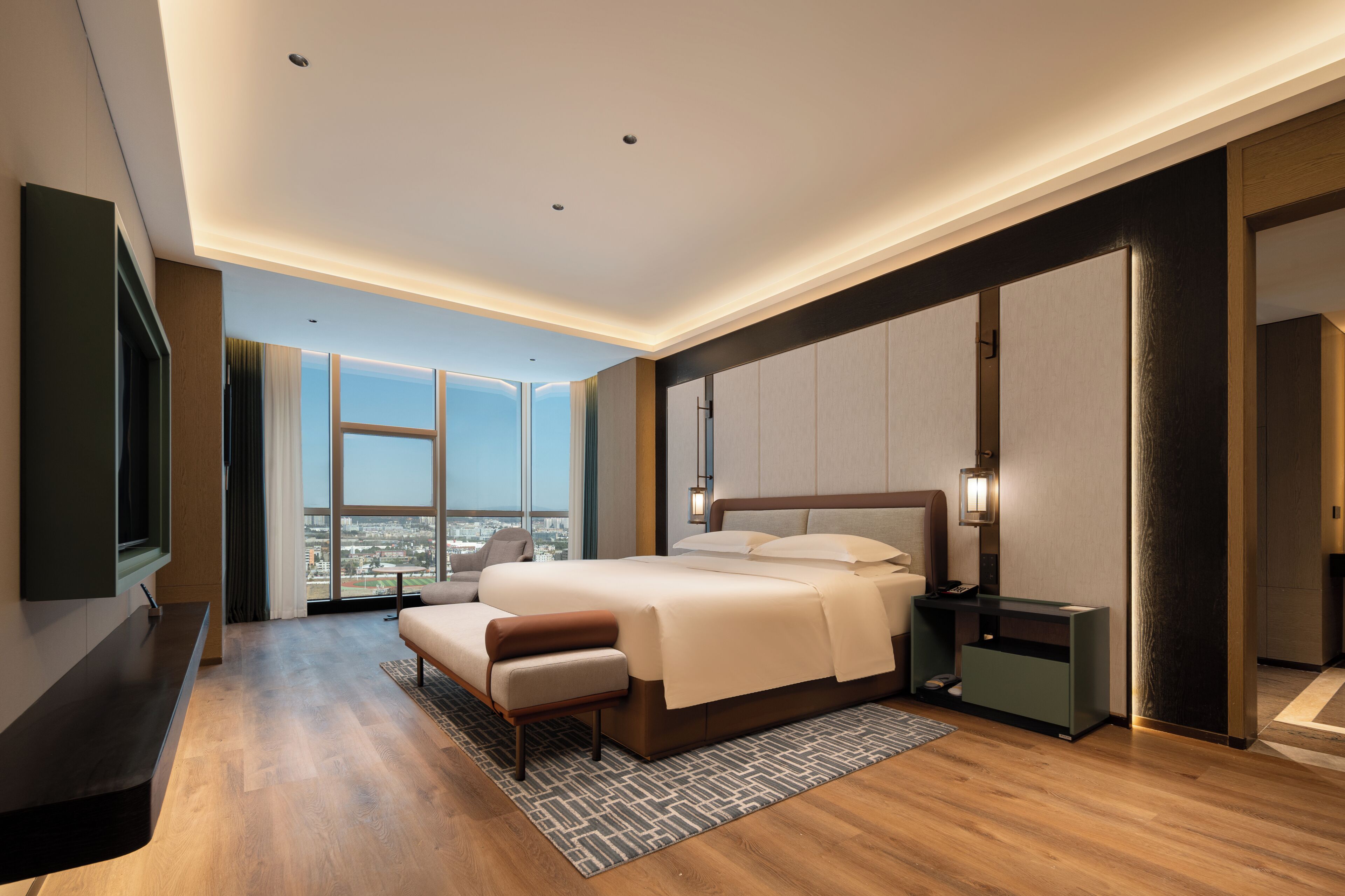 Ein modernes Hotelzimmer mit einem großen Bett, einem Schreibtisch, einem Stuhl und Blick auf die Stadt.