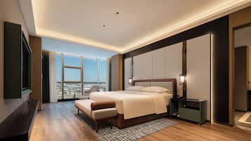 A modern hotel room with a large bed, a desk, a chair, and a view of the city.