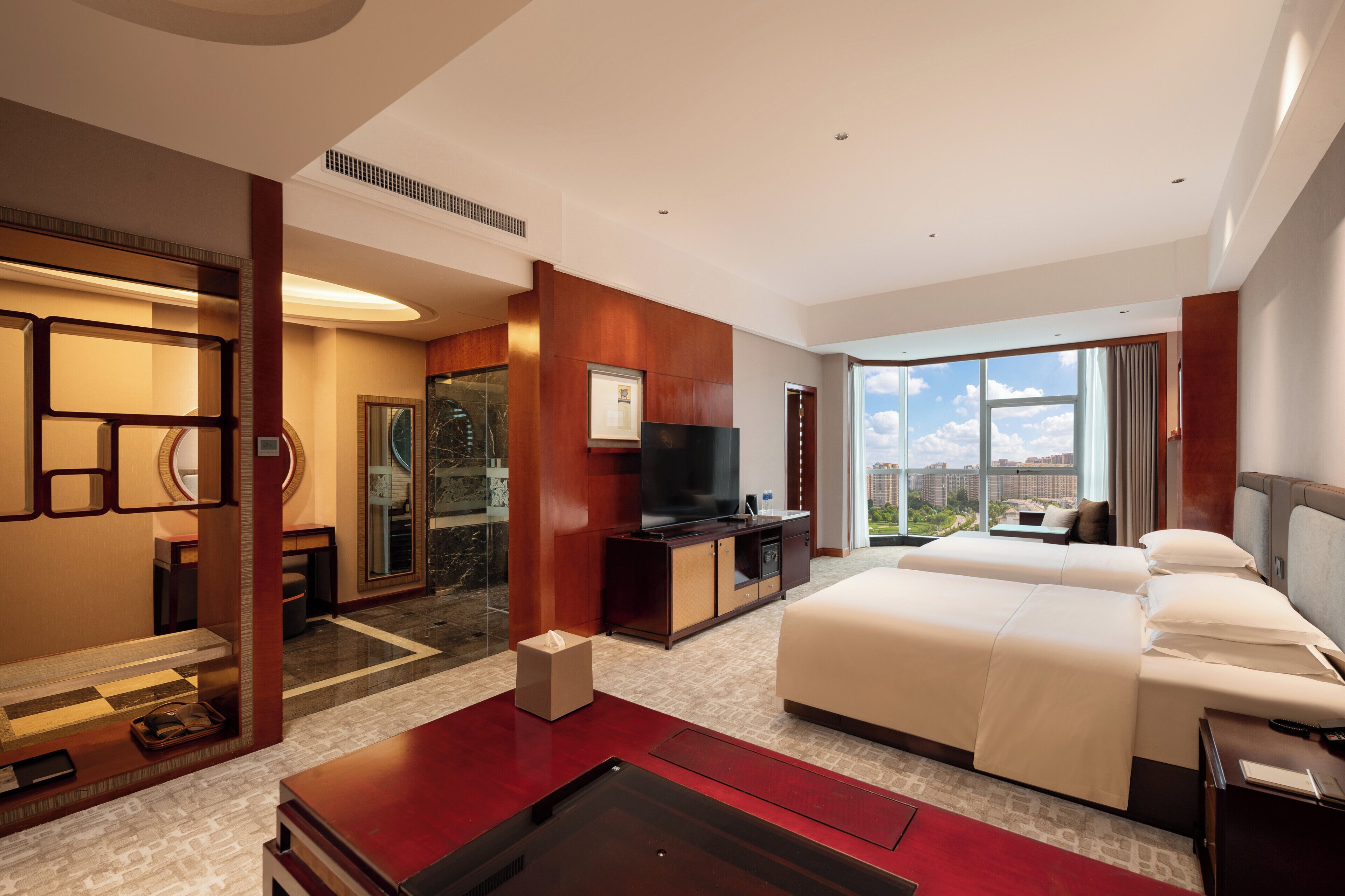 A hotel room with a large bed, a desk with a flat-screen TV, a seating area with a view, and a large window.