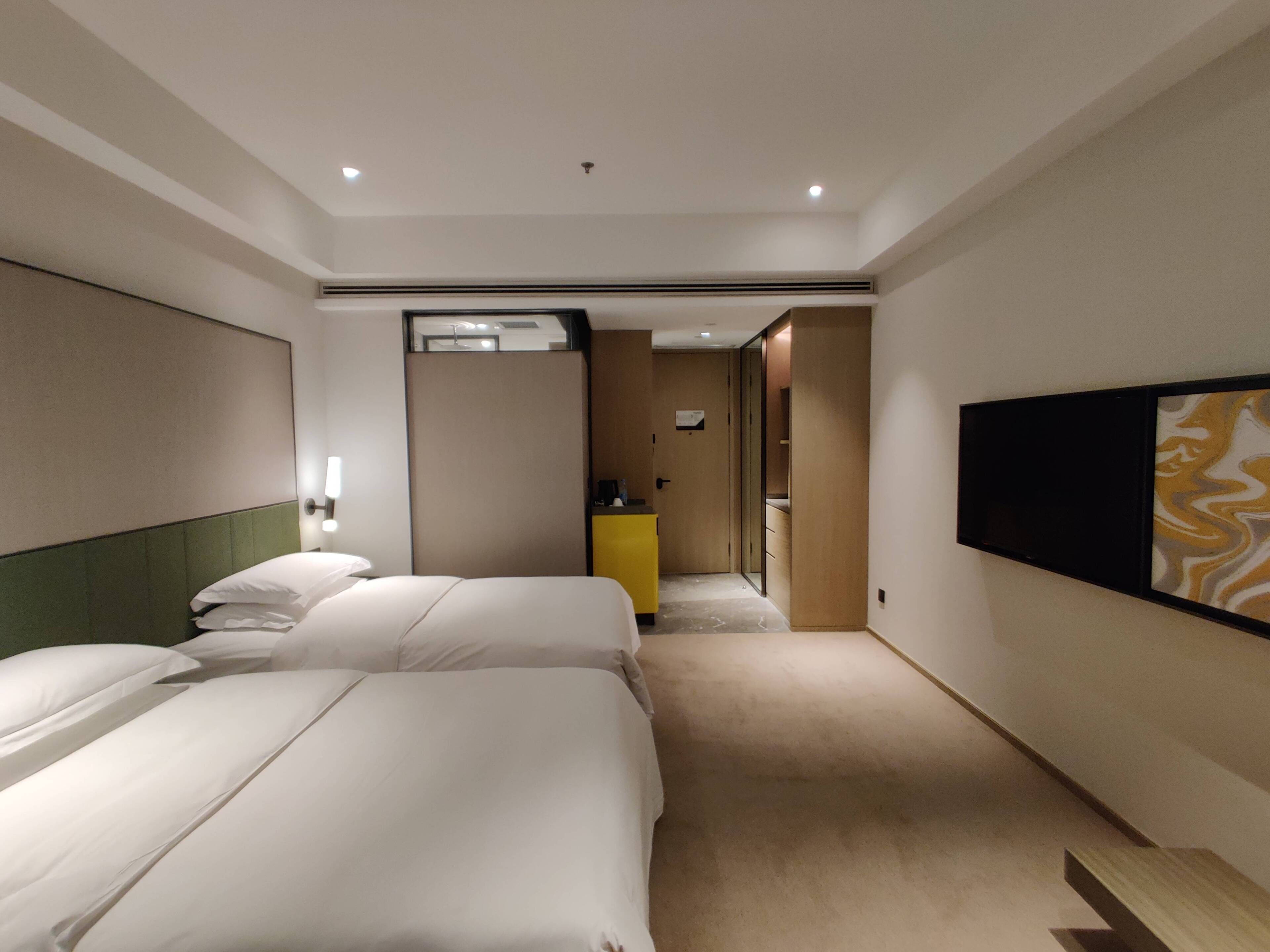 A hotel room with two beds, a bedside table, a mirror, a wardrobe, and a TV mounted on the wall.