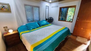 Un dormitorio con cama, mesita de noche, ventilador y ventana.