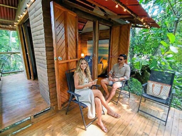 A wooden cabin with a porch, two chairs, and a bag on a bench.