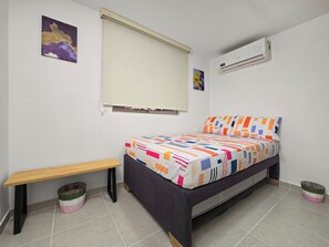 Ein Schlafzimmer mit Bett, Sitzbank, Mülleimer und Klimaanlage.