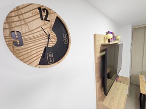 Une horloge murale en bois, avec un cadran noir et des chiffres dorés, fixée au mur au-dessus d’un téléviseur à écran plat.