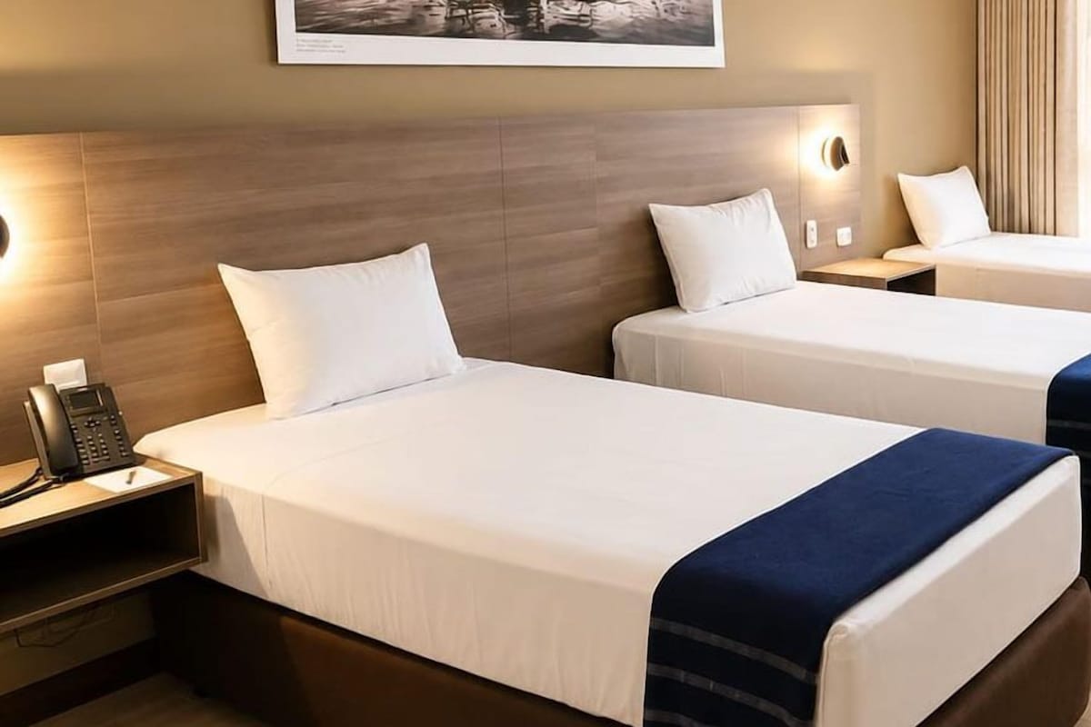 A hotel room with two beds, a bedside phone, and a wall-mounted light fixture.