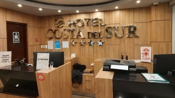 A hotel reception desk with a wooden panel wall and a sign reading 'HOTEL COSTA DEL SUR'. - Hotel Costa del Sur (Ilo)