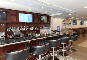 Una zona de bar con una barra larga, varios taburetes y una pantalla de televisión.