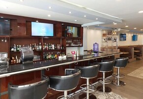Una zona de bar con una barra larga, varios taburetes y una pantalla de televisión.